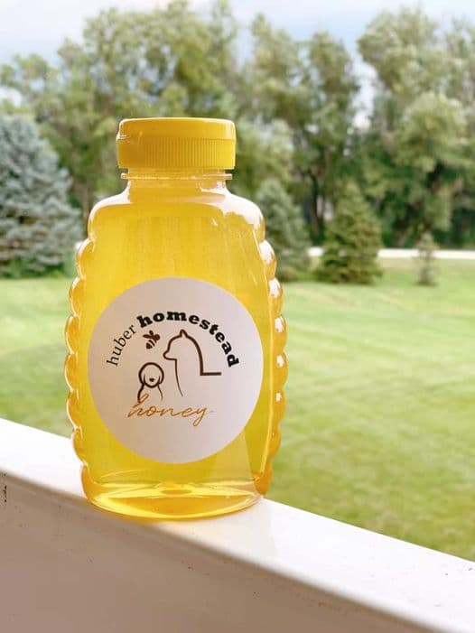 Golden honey in a beehive-shaped bottle with a Huber Homestead label on a white railing.